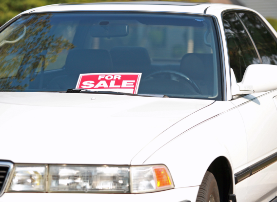 Front view of a white car with a for sale sign in the windshield.